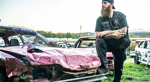 Man with foot on the front fender of a demolition derby car