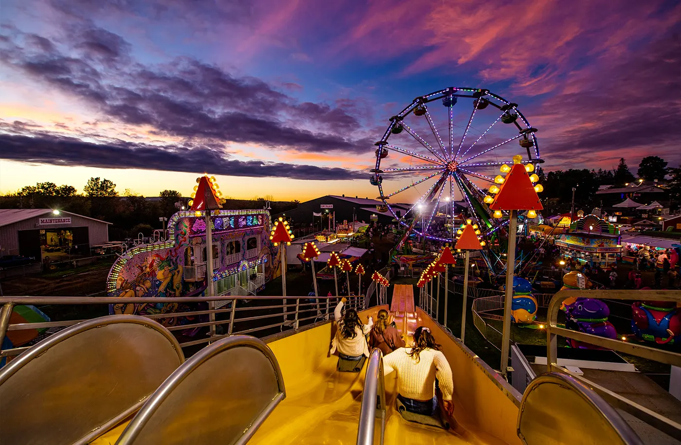Night view of rides at the fair including a slide and Ferris wheel